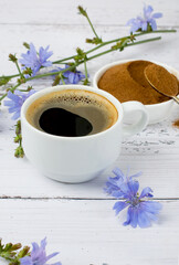 Ground chicory root in a bowl, cup with drink, chicory flowers and sprigs on a wooden light...