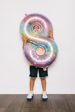 Happy Child Hidden Behind Number 8 Balloon in Studio Setting