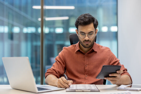 Serious concentrated hispanic businessman financier on paperwork inside office, man in business suit at workplace reviewing and reading papers, contracts and accounts reports