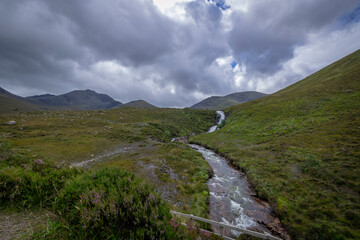 A serene stream meandering through lush green grass under a cloudy sky in a beautiful outdoor landscape.  Scotland, landscape