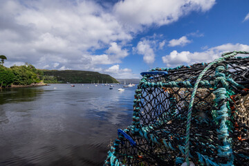 A serene landscape featuring a body of water with boats and buildings along the shore. The image captures a peaceful scene with a cloudy sky overhead.  Portree, Scotland, isle of skye