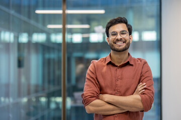 Confident young businessman smiling with arms crossed in modern office environment showcasing...