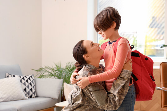 Military mother hugging and getting her little son ready for school in living room