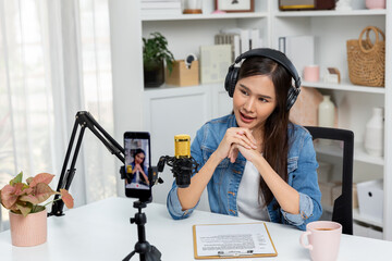 Host channel Asian influencer talking in broadcast wearing headsets on social media live on smartphone recording online, greeting listeners with coaching life or business at modern studio. Stratagem.