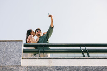 Couple taking a selfie on a balcony, capturing a sweet moment