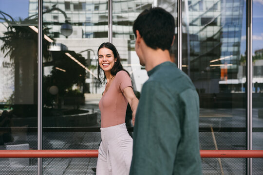 Woman smiling at man while walking in modern urban area