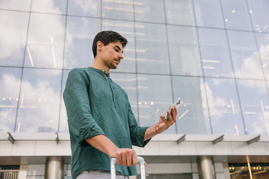 Man with suitcase using smartphone outside modern building in Azca