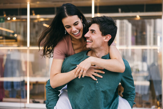 Joyful piggyback ride of a couple smiling in Azca, Madrid street