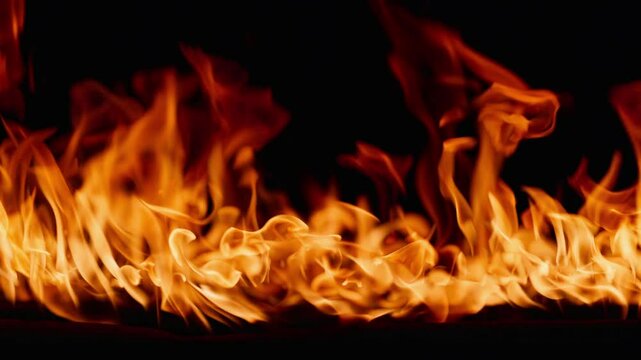 Beautiful dancing fire, the surface is ablaze. Lots of fire. Close-up immersion in the flames. The camera passes through the fire. Burning tongues of flame on a black backdrop in slow motion