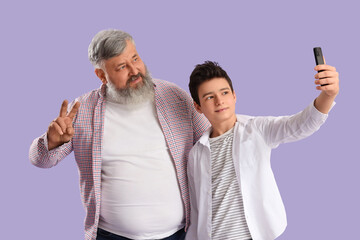 Happy grandfather with his cute grandson taking selfie on purple background