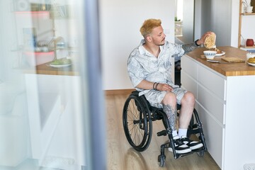 Man in wheelchair placing coffee cup on kitchen counter with baked goods in background and modern...