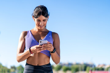 A woman in athletic wear smiles while looking at her smartphone