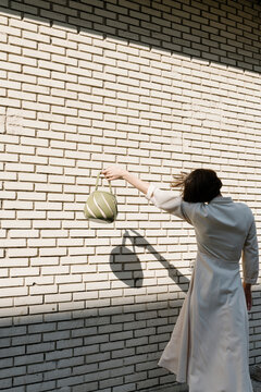 Woman Holding Handbag Against White Brick Wall in Sunlight