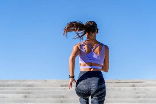 A woman with long hair in a ponytail running up concrete steps outdoor
