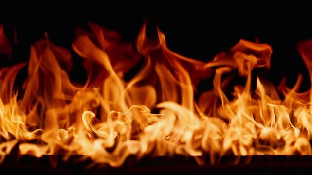 Beautiful dancing fire, the surface is ablaze. Lots of fire. Close-up immersion in the flames. The camera passes through the fire. Burning tongues of flame on a black backdrop in slow motion