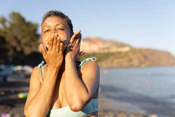 A MATURE WOMAN USING SUN CREAM ON THE BEACH