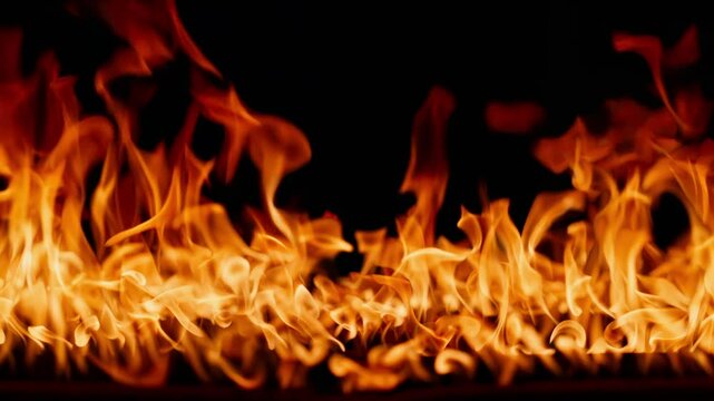 Beautiful dancing fire, the surface is ablaze. Lots of fire. Close-up immersion in the flames. The camera passes through the fire. Burning tongues of flame on a black backdrop in slow motion