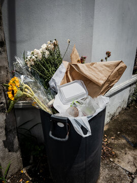 Dead flower bouquets in a streetside trash bin in Bangkok