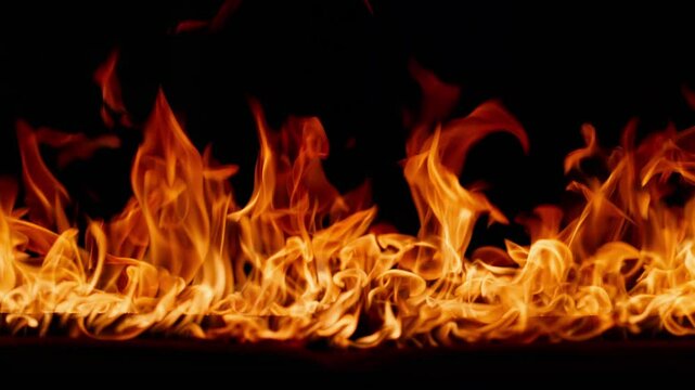 Beautiful dancing fire, the surface is ablaze. Lots of fire. Close-up immersion in the flames. The camera passes through the fire. Burning tongues of flame on a black backdrop in slow motion