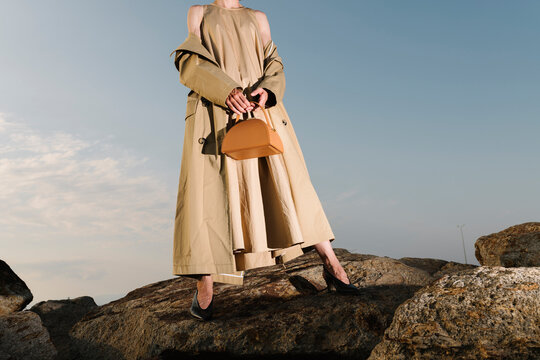 Elegant Woman in Beige Trench Coat Holding Brown Handbag Outdoor