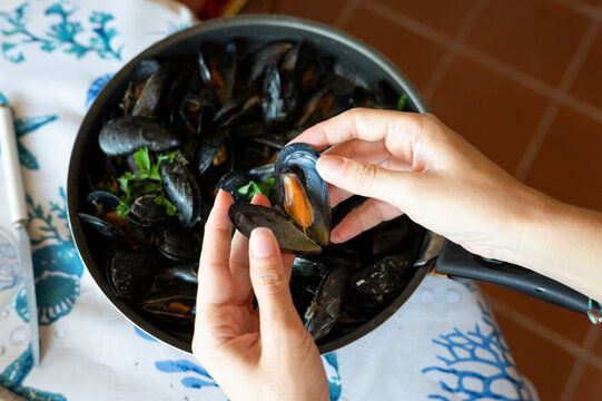 Hands Holding Cooked Mussel Above Pan