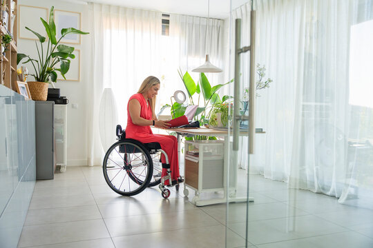 Professional woman in wheelchair working on laptop at home office