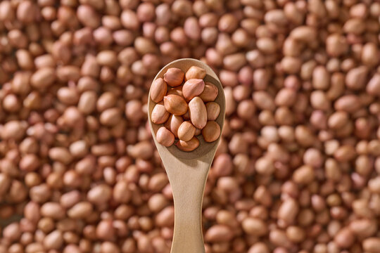 Wooden Spoon Holding Peanuts Against Blurred Background