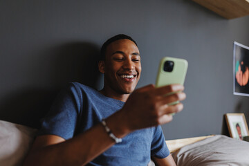 Happy man using smartphone and relaxing in bed