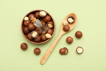 Bottle of macadamia oil and nuts in bowl on green background