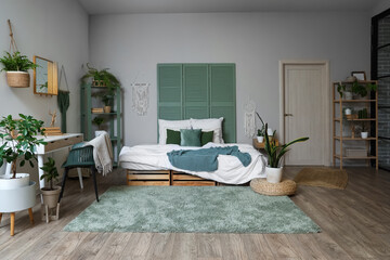 Interior of stylish bedroom with cozy bed, workspace and houseplants