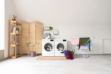 Interior of bathroom with washing machines, dryer and laundry basket