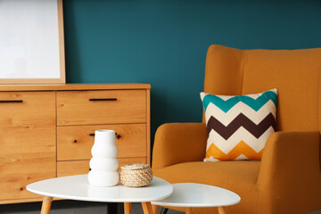 Home decor on coffee table near armchair and commode against blue wall