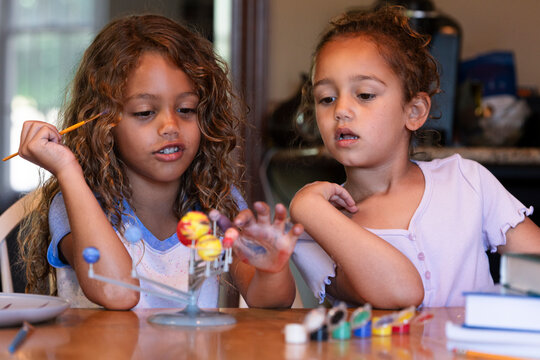 Young Sisters Painting Solar System Model Together
