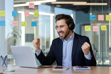 Excited businessman celebrating success at computer with headphones on