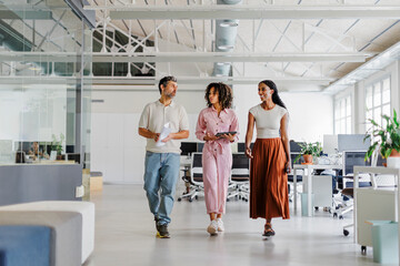 Three business people walking and talking in modern open plan office