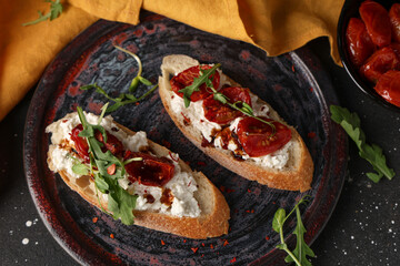 Plate of tasty tomato bruschetta with ricotta and arugula on black background