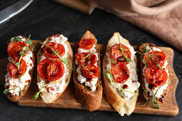 Wooden board of tasty tomato bruschetta with ricotta on black background
