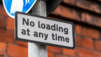 Obraz premium Close-up of a 'No Loading at Any Time' Sign on a Metal Pole Against a Brick Wall