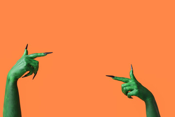 Green hands of witch pointing at something on orange background. Halloween celebration