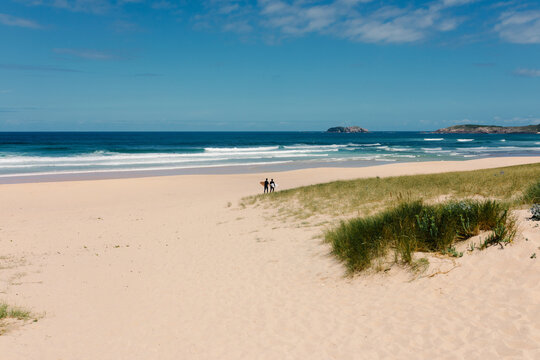 Long shot depicts surfers strolling in the distance on Doni&ntilde;os beach