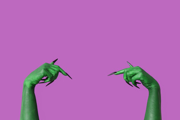 Green hands of witch pointing at something on purple background. Halloween celebration