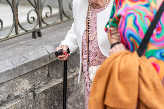 Elderly woman using walking stick with nurse assisting