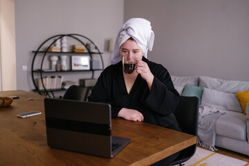 Plus size woman drinking coffee and watching show on laptop in room