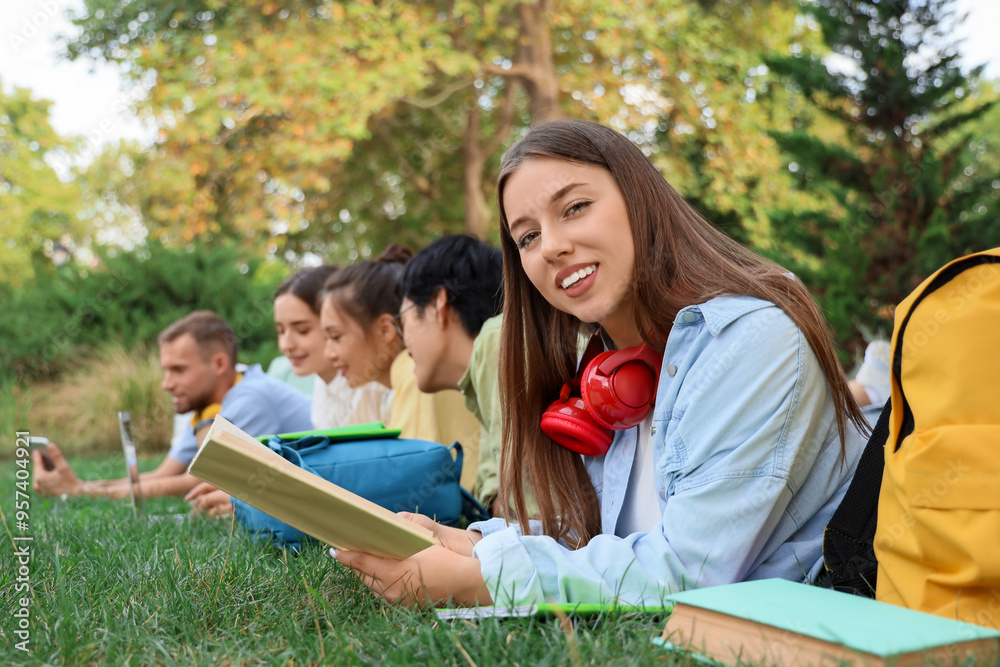 Sticker Female student with book and her classmates lying on grass in park