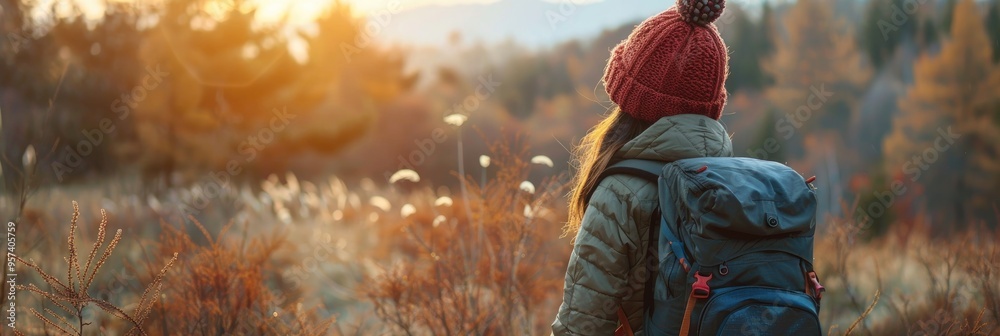 Canvas Prints woman hiking in a vibrant autumn forest with a backpack and knitted hat while appreciating the sunri