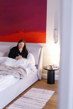 Plus size woman making notes in her notebook sitting in bed