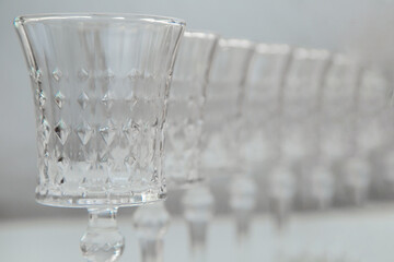 Crystal wine glasses with expanded edges and faceted pattern stand in a row on a white background, the first one is in focus on the sides, the second ones stand behind it in focus, close-up, the legs