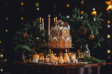 Family holiday celebration. Beautiful traditional homemade gingerbread house. Celebration of Christmas and Happy new year at home. Festive mood, cozy atmosphere, burning candles, fir tree branches