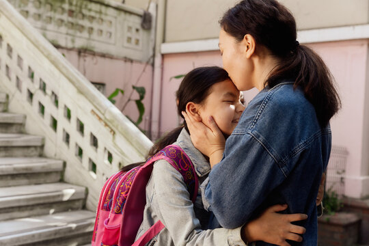 mom hugs and kiss happy daughter near school
