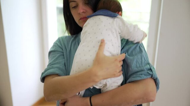 Mother struggles to burp newborn baby over her shoulder, visibly uncomfortable as the infant complains